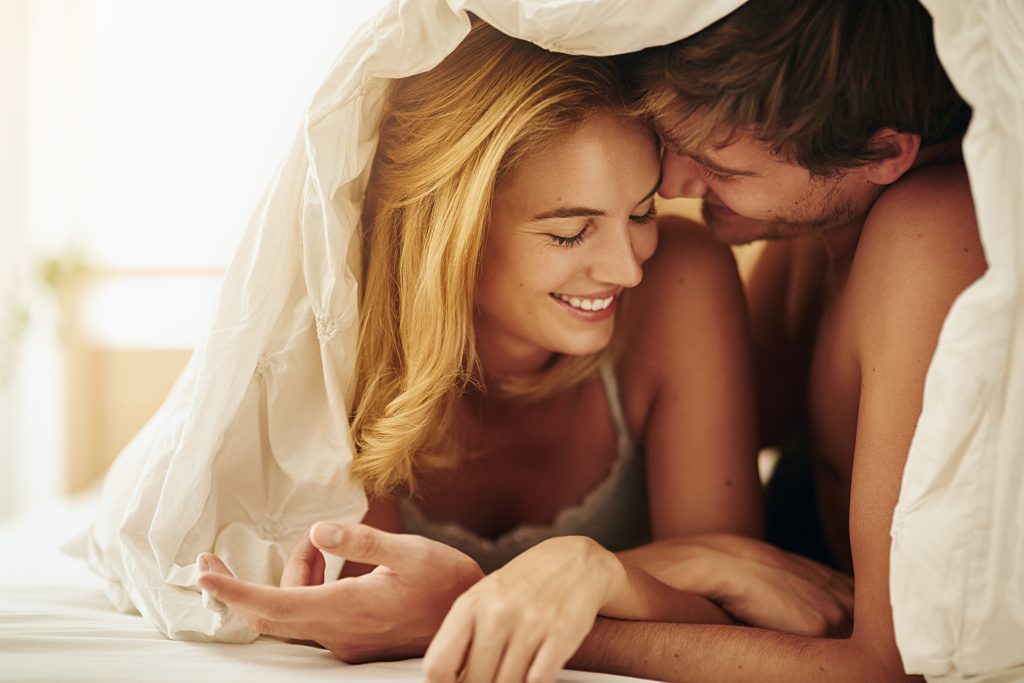Couple smiling together under white sheets in bed