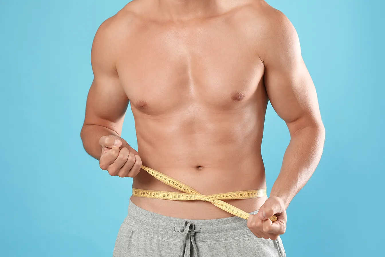 Man measuring his waist with a tape measure to track abdominal contour.